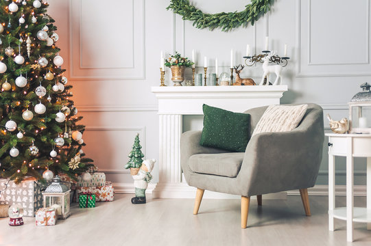 Classic interior with an armchair tables, and a Christmas tree with decorations on a light background of a wall with a fireplace.