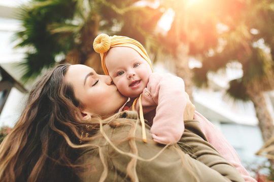 Incredibly beautiful mother holding in her arms her daughter and kissing outside. Fashionable stylish look.