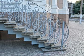 gray concrete steps and iron handrails with a forged pattern on the sidewalk near the wall of the...