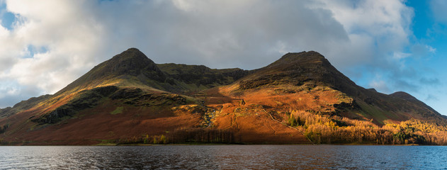 Majestic vibrant Autumn Fall landscape Buttermere in Lake District with beautiful early morning sunlight playing across the hills and mountains