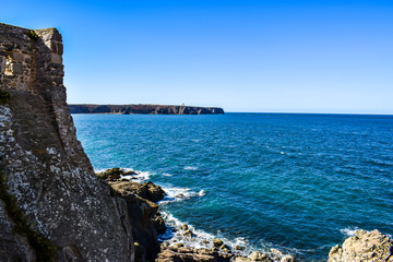 Fototapeta na wymiar vu du fort la latte vu au loin le cap Fréhel et son phare, l'océan vert émeraude, château fort situé sur la pointe de la Latte, dans le département des Côtes-d'Armor 