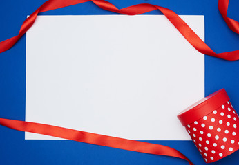 Fototapeta premium empty white sheet of paper and red silk twisted ribbon on a blue background