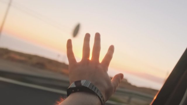Man's hand reaches for the sun out of the car windows, slow motion . The last rays of the setting sun