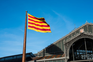 Fototapeta na wymiar Flag of Catalonia. Senyera. Red and yellow striped flag and on clean blue sky background. Flag waving in the wind in sunny day. Old building on background.