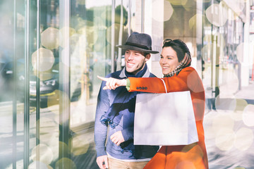 Young man and woman dressed in winter clothing window shop during the holiday season - Pointing and...