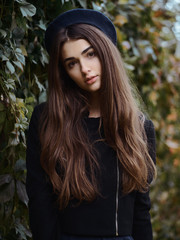 Naklejka premium Mood contrasty portrait young elegant french style brown haired woman in beret and black leather jacket enjoying free time strolling in fall city park cinematic stock colour grading ivy background