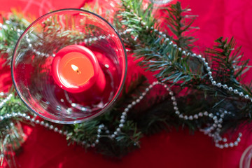 Table setup lunch in red for celebration. Shiny glass cup, red tablecloth, candles and decorations with green Christmas tree. Christmas dinner during the holiday decorated table. Dining table setup