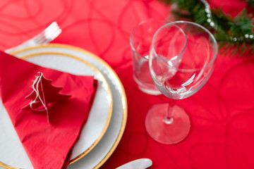 Table setup lunch in red for celebration. Shiny glass cup, red tablecloth, candles and decorations with green Christmas tree. Christmas dinner during the holiday decorated table. Dining table setup