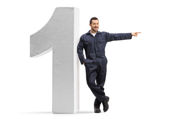 Male worker in an overall uniform leaning on a big number one and pointng to the side