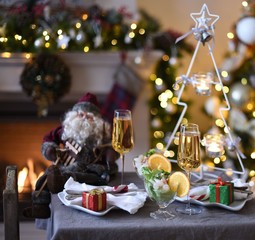 decorated New Year's table or Christmas table  . Closeup of two glasses of champagne in front of burning fireplace