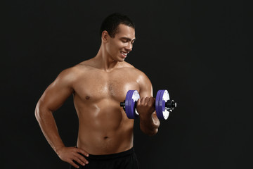 Sporty African-American man with dumbbell on dark background