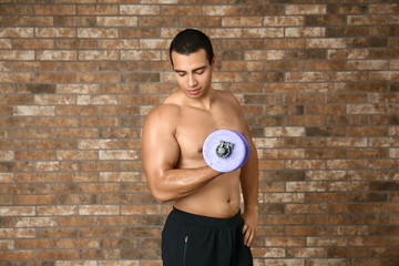 Sporty African-American man with dumbbell on brick background