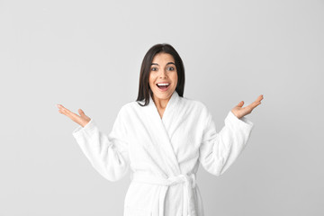 Surprised young woman in bathrobe on grey background
