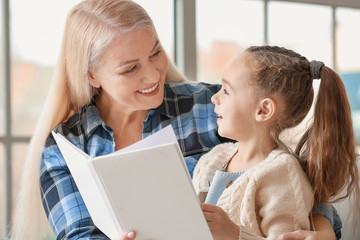 Little girl and grandmother reading book together at home