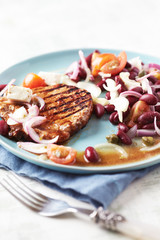 Grilled pork steak with Kidney bean, cherry tomatoes, onion and capers on bright wooden background