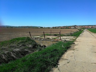 Bridge old with iron railing, across a ditch between a panel road and a field