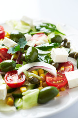 Healthy salad with green olives, feta cheese, sweet corn, cherry tomatoes, red onion, baby spinach, capers and fresh herbs. Close up.