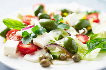 Healthy salad with green olives, feta cheese, sweet corn, cherry tomatoes, red onion, baby spinach, capers and fresh herbs. Close up.
