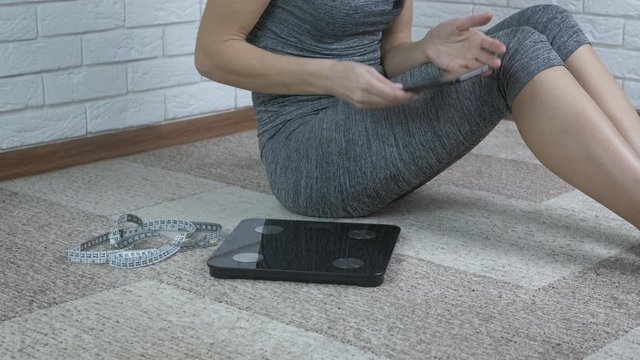 Check body weight. A woman on a smartphone to calculate her weight, gets on the scales.