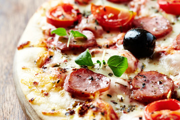 Pizza with sausage, cherry tomatoes, black olives and fresh herbs. Home made food. Concept for a tasty and hearty meal. Close up. 