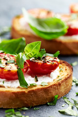 Crostini withe cream cheese, cherry tomatoes and fresh basil. Dark stone background. Close up.