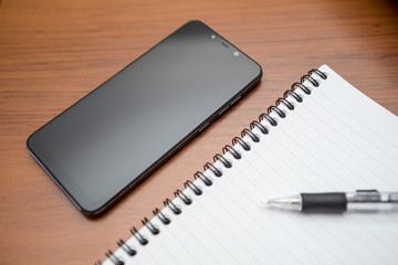 Notebook, mechanical pencil and smartphone with black screen on wooden table.