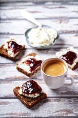 Cup of coffee and sandwiches with cream cheese and jam. White wooden background.