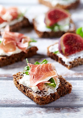 Tasty sandwiches with cream cheese, smoked ham and figs. Bright wooden background.