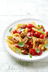 Penne pasta with cherry tomatoes, chicken breast and fresh basil. Bright wooden backgroudn. 