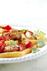 Penne pasta with cherry tomatoes, chicken breast and fresh basil. Bright wooden backgroudn. Close up. 