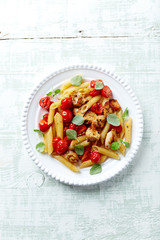 Penne pasta with cherry tomatoes, chicken breast and fresh basil. Bright wooden backgroudn. Top view. Copy space. 