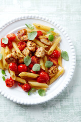 Penne pasta with cherry tomatoes, chicken breast and fresh basil. Bright wooden backgroudn. Top view.