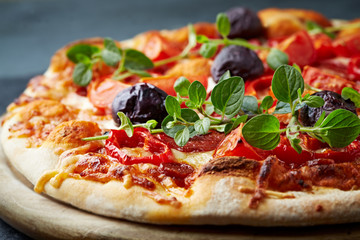 Pizza with mozzarella cheese, cherry tomatoes, black olives and fresh oregano. Home made food. Concept for a tasty and hearty meal. Black stone background. Close up. 