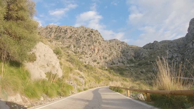 POV footage of car driving through beautiful rocky mountain landscape and pine forest. Winding road on Mallorca island, Baleares, Spain. Epic 4K real time video during sunset. Point of view 