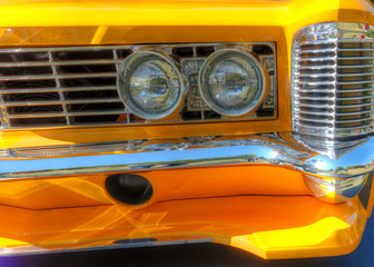 A very closeup shot of the front headlights on a yellow vintage sports car