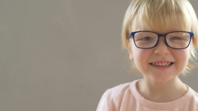 Portrait of funny blond child in new glasses. Boy puts on and adjusts glasses
