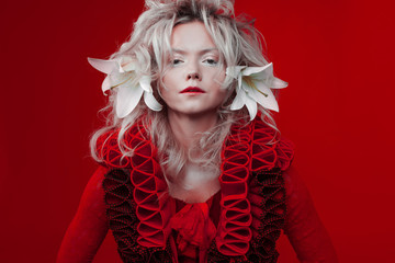 Shades of red. Attractive woman, in a red dress, posing on a red background, with white lily flowers in her hair.