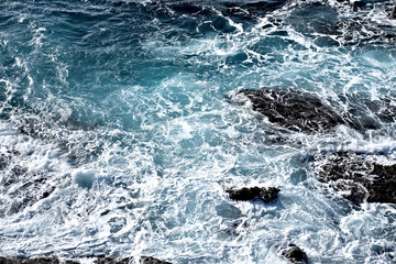 Stormy ocean waves, deep blue sea water with white foam and dark dangerous rocks.