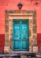 A beautifully restored vintage door painted turquoise with a stone frame and red wall