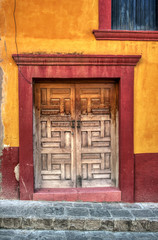 A wooden door that has been partly varnished with a concrete red frame  and orange wall