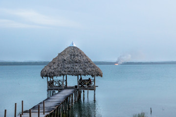Dock at lake Itza with wild fire in the back, El Remate, Peten, Guatemala