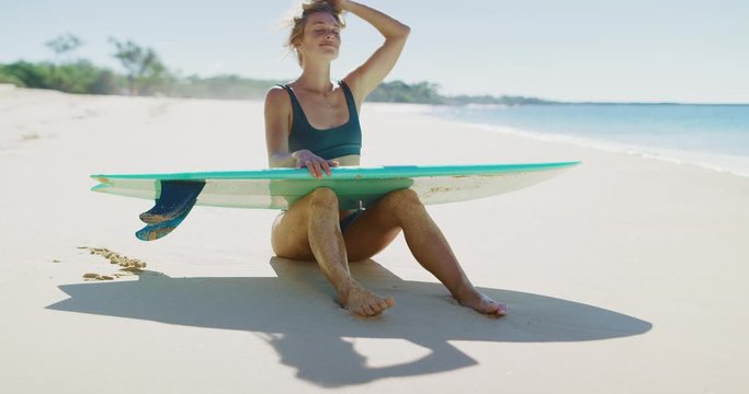 Happy active surfer girl holding her blue surfboard on a sunny tropical beach, smiling young woman radiating health and wellness