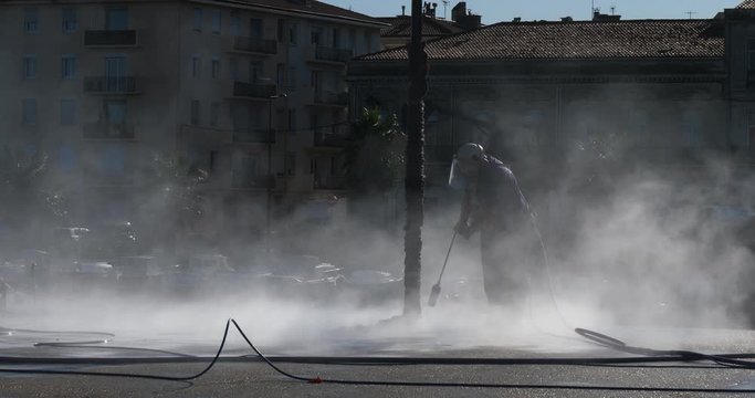 Worker cleaning a pavement with using a hight pressure cleaner.