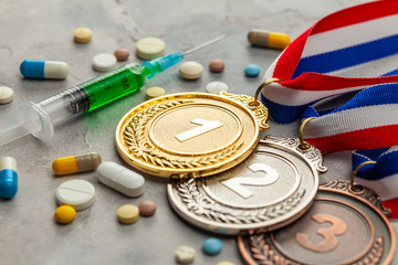 Doping for athletes. Golds, silver and bronze medal and doping syringe and pills with capsules on a gray background - obrazy, fototapety, plakaty