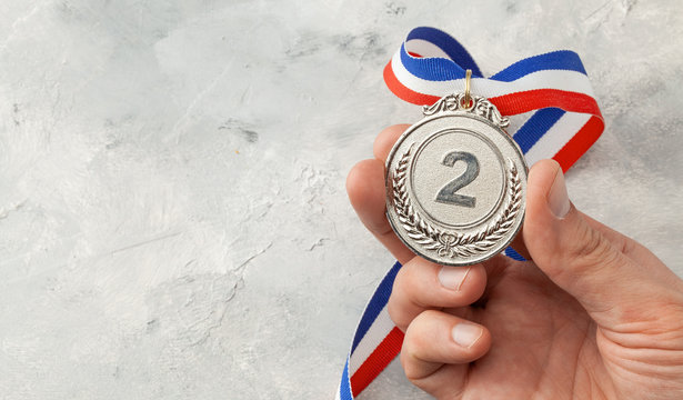 Silver Medal. The Second Place Award With A Ribbon A Man Holds In His Hand