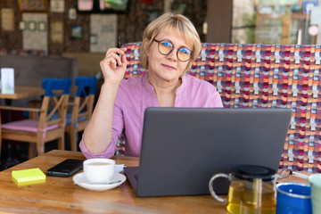A woman with a laptop looks at a document in a cafe, office