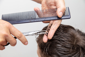 Hairdresser cuts the hair of a boy with scissors