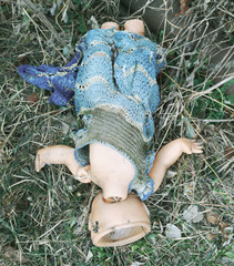 An old headless doll lies on the ground
