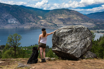 girl standing on a rock cliff her beloved dog on a leash with a panoramic view of the mountains of the okanagan valley