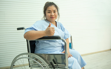 Asian fat woman sitting on wheelchair and raised thumb up.